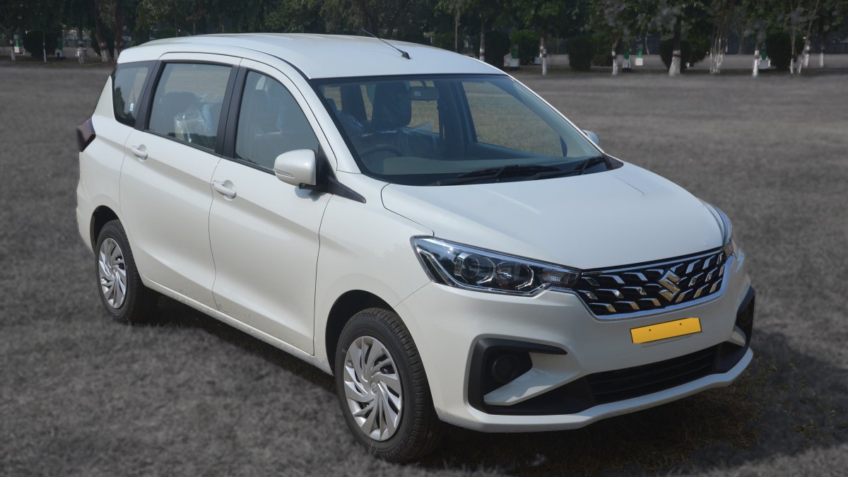 A white Ertiga operated by Jain Cabs, 7+1 seats, photographed on a clear road with its yellow commercial number plate visible.